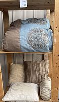 Comforter folded on upper shelf and decorative pillows arranged on lower shelf of wooden shelving unit.