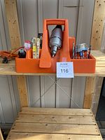 Vintage Black & Decker all metal drill with its orange plastic carrying caddy on a wooden shelf.