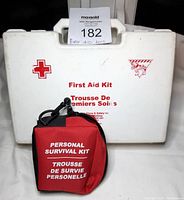 Closed view of the full size white plastic first aid kit with red cross and text alongside the red personal survival kit pouch with clip attachment.
