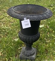 Front angle view of large cast iron garden urn showing ornate petal detailing on lip and rounded base section with square pedestal base.