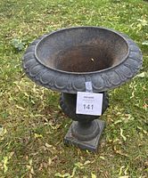 Top angled view showing the ornate cast iron rim and rusted interior surface of the garden urn sitting on grass.