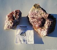 Two amethyst crystal pieces on rock displayed side by side with note card for size reference.