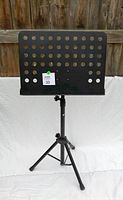 Front view of the black metal music stand showing the perforated sheet holder with adjustment knobs and tripod base.