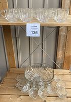 Punch bowl sets displayed on wooden shelves, one set on the top shelf includes 12 ribbed clear glass cups, the lower shelf contains a ribbed punch bowl and a starburst patterned punch bowl with 12 matching starburst patterned cups arranged around it.