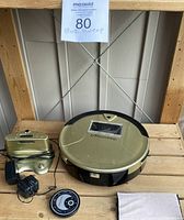Top view of Bobsweep vacuum with charging dock, power adapter, remote control, and cleaning cloth on wooden surface.