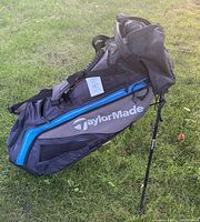 Side view of gray and blue TaylorMade golf stand bag showing built-in stand legs and TaylorMade branding.