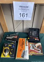 Overall view of assorted tools laid out on a wooden surface, including measuring tools, wrench set, staple gun, and black case with bits
