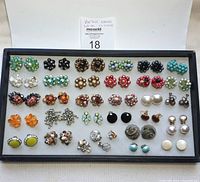 Full lot view of 33 vintage earrings arranged on gray felt tray in two rows with varied colors and styles