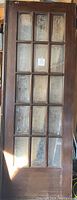 Full view of one vintage solid wood French door with 15 frosted glass panes showing fleur-de-lis etching.