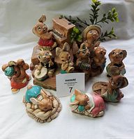 Front view of 13 vintage Pendelfin and Tinker Ware bunny figurines arranged with large wooden base and greenery branch