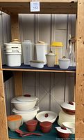 Overview of the lot on shelves showing white, beige, and yellow Tupperware containers, glass bottles, bowls, and serving utensils.
