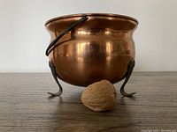 Front angle view of the round 1960s copper planter showing the wide top opening, natural copper color, and curved wrought iron feet with the handle visible.