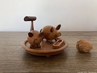 Front view of two pig shakers on round wooden tray with handle and trough container, plus walnut for size reference