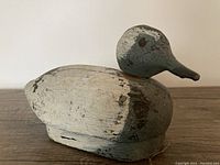 Side view of wooden duck decoy showing weathered white, gray, and black paint with heavy chipping and aging on the body and head.