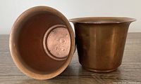 Two small solid copper flower pots, one upright and one upside down, showing the interior and shape.