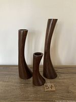 Front view of three sculptural Danish teak candleholders in varying heights on wood surface