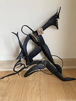 Angled view of abstract brutalist metal wall sculpture in black with curved and pointed elements, sitting on floor against wall