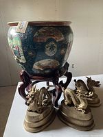 Large blue porcelain fish bowl with Asian hand-painted scenes and floral decorations on wooden stand with three metallic dragon figurines in front