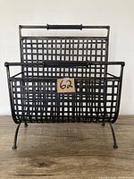 Front view of vintage metal magazine holder showing basket weave design and tubular handles.