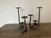 Pair of iron brutalist metal candleholders on wooden table, showing side view with twisted rods and spherical detail under medium-height candle cup