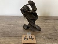 Front view of the vintage bronze sculpture on a wooden surface with lot number 64 visible.