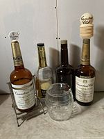 Photo of four vintage liquor bottles including Canadian Club with brass cradle, McGuinness Gold Tassel, Hiram Walker & Sons, and clear glass barrel with spigot.