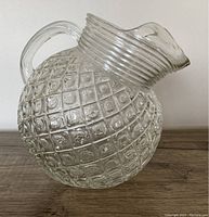 Side profile of the clear glass tilt pitcher showing the diamond waffle pattern, ribbed neck, integrated handle, and pouring spout.