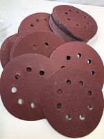 Stack of maroon 5-inch sanding discs showing multiple dust extraction holes on abrasive side.