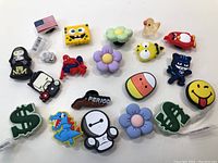 Top view of 20 assorted colorful shoe charms laid out on white surface.