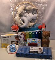 Lot display photo showing multiple baby items including plush teething ring, Fisher-Price xylophone, Medela Quick Clean wipes, pacifiers, Toolik diaper bag refills, brown fox-shaped bottle warmer, and baby bottle nipple.