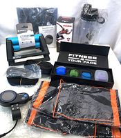 Photo showing the assortment of fitness items including hand grip, shaker bottle, electronic pulse massager, massage balls in box, gloves, and straps