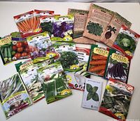 Photo showing a variety of sealed seed packets spread out on a surface. Includes carrot, lettuce, sweet pea, parsley, onion, and other vegetable and herb seeds from brands including McKenzie and Italia.