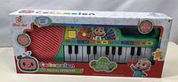 Photo showing the Cocomelon Musical Keyboard in its original packaging, featuring 23 keys and colorful character designs.