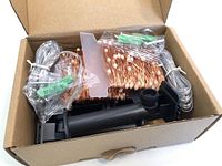 Opened box showing coiled copper wire string lights, solar panel, and mounting stake packed inside a cardboard box.