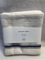 Two folded cream kitchen towels with navy blue stripes, original packaging band showing brand and product details.