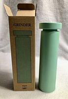 Photo showing matte green HAY grinder standing next to its original packaging box.