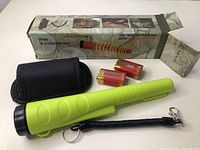 Metal detector and accessories arranged next to product box showing product image and accessory list.