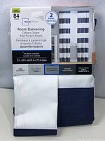 Front of packaging showing product name, size, panel count, and fabric details with white and navy folded curtains visible