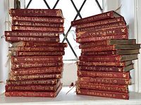 Two stacks of red leather bound Shakespeare volumes arranged on a windowsill
