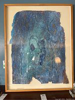 Full view of the framed sculpted paper artwork showing textured blue-green abstract design, within a wooden frame under glass.
