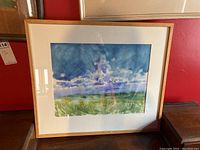 Full view of framed watercolour painting depicting a landscape with cloudy sky and field, housed in a wooden frame with glass.