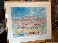 Full view of framed watercolour painting showing landscape with hills and blue sky.