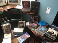 View of assorted CDs and VHS tapes on wooden desks and chairs, showing mixed media and cases.