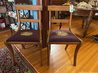 Two matching wooden chairs with floral needlepoint seats, shown straight on.