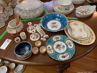 Table top with assorted ceramic and glassware items including a blue floral bowl, turquoise floral plate, white and gold edged plates, and small pottery pieces.