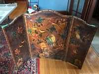 Front view of the three-panel folding fireplace screen showing detailed painted birds and floral artwork with signs of wear and aging.