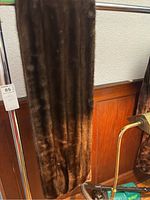 Full length view of the dark brown fur stole hanging on a rack, showing its glossy fur texture and length.