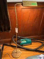 Full view of brass floor lamp with Hoover vacuum cleaner behind it on wood floor, showing lamp height and base.