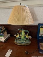 Photo of entire table lamp placed on wood surface showing beige pleated fabric shade and colorful bird-themed porcelain base.