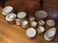 Full assortment of stacked dinnerware, multiple plates, cups, bowls, and gravy boat on wooden floor